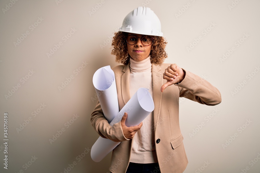 African american curly architect woman wearing safety helmet and glasses holding blueprints with angry face, negative sign showing dislike with thumbs down, rejection concept African american curly architect woman wearing safety helmet and glasses holding blueprints with angry face, negative sign showing dislike with thumbs down, rejection concept