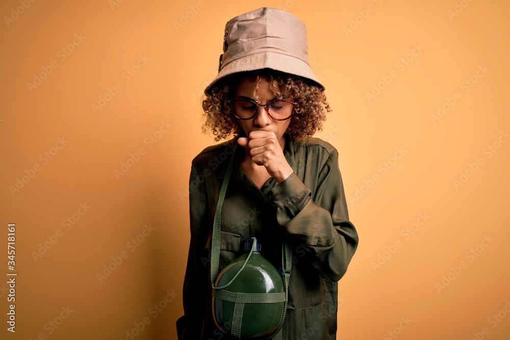 Young african american tourist woman on vacation wearing explorer hat and water canteen feeling unwell and coughing as symptom for cold or bronchitis. Health care concept. Young african american tourist woman on vacation wearing explorer hat and water canteen feeling unwell and coughing as symptom for cold or bronchitis. Health care concept.