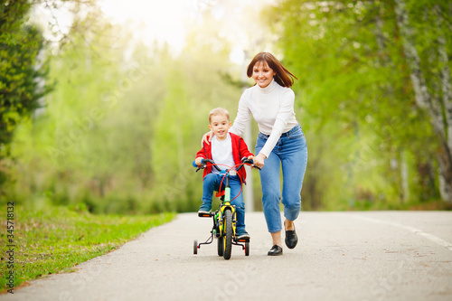 Little boy learns how to ride bicycle, his Mom is happy and laughs success. Concept family, support