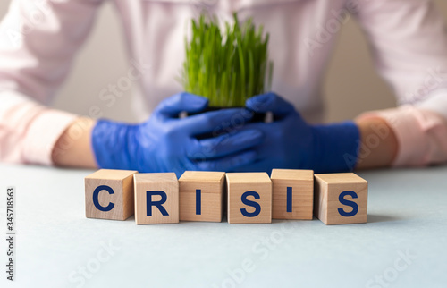 crisis inscription on wooden cubes on light rable with blurring background of protective gloves and grass. Crisis ecology medicine and economic concept photo