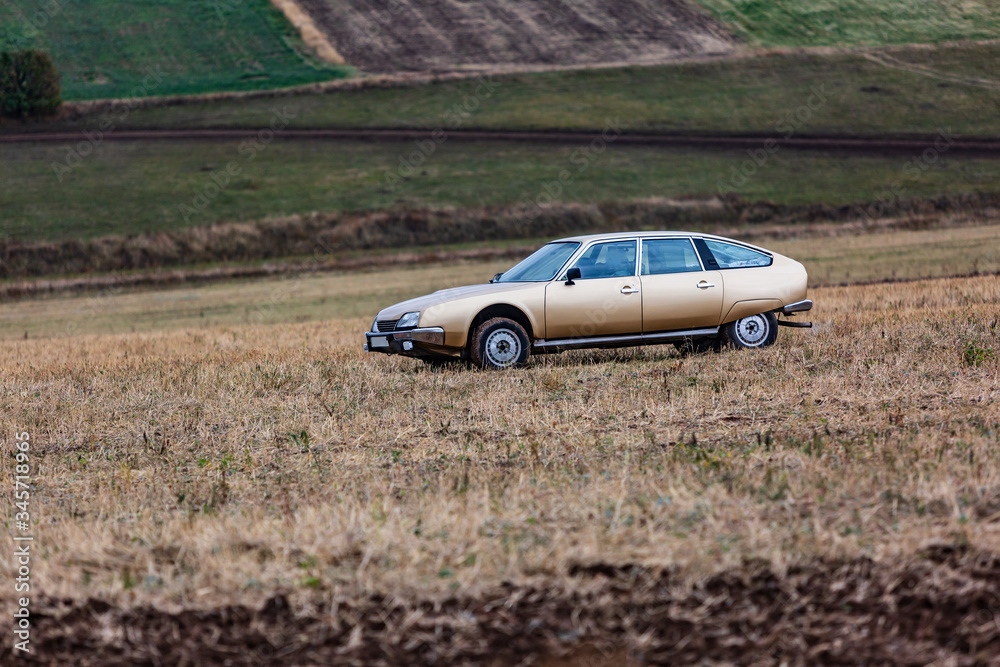 A beige car stands in a field against the background of other fields and land on a cloudy day. Horizontal orientation.
