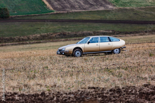 A beige car stands in a field against the background of other fields and land on a cloudy day. Horizontal orientation. © Sander Studio
