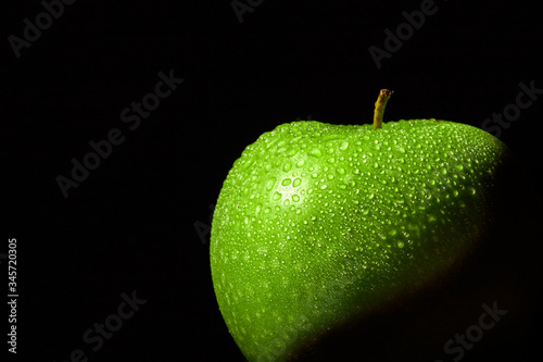 Fresh green apple with water droplets on black background. Close-up macro photo concept for green fruits, freshness, healthy nutrition. Conceptual background. 