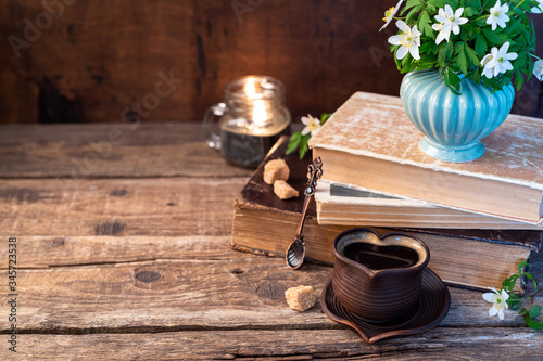 Bouquets of forest flowers, coffee cup, old books, candle on wooden rustic table. Cozy home, breakfast, reading, hygge, evening, comfort, rest concept. Mysterious home interior. Copy space