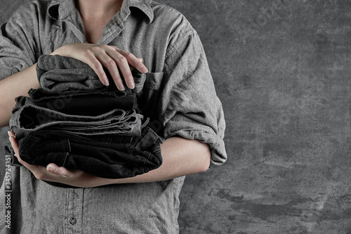 Female hands hold stack of neatly folded dark clothes isolated on black gray background close-up