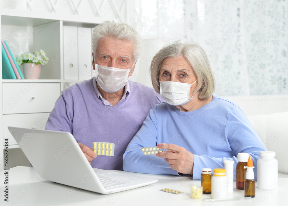 Ill senior couple with facial masks using laptop