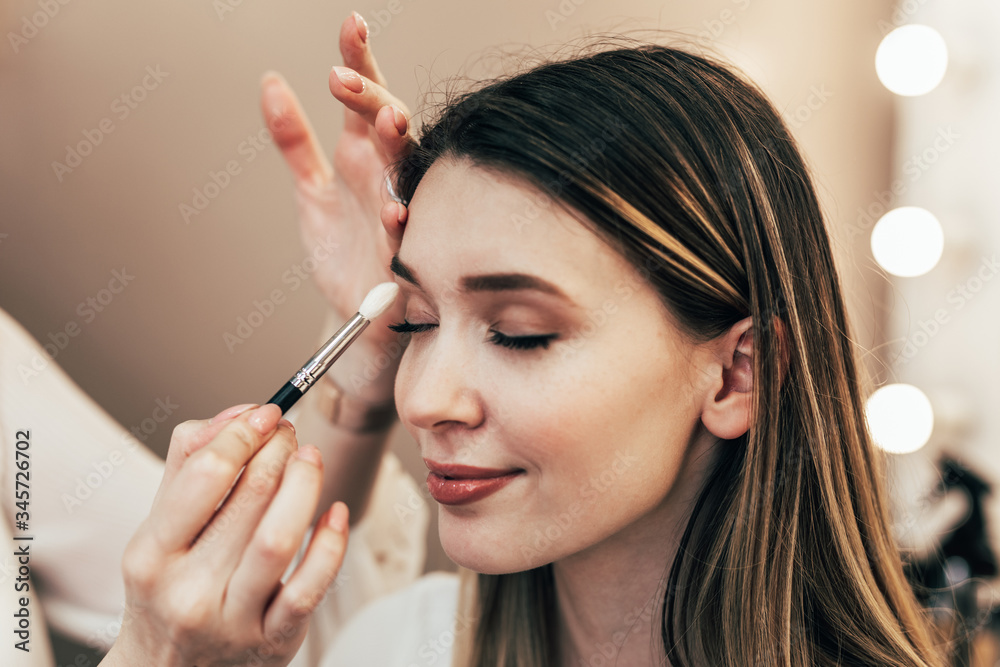 Fototapeta premium Make up artist doing professional make up of beautiful young woman.