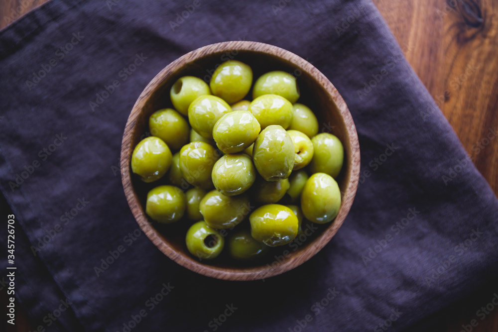 Green olives in a wooden bowl on a table, top view. Green olives in a wooden bowl on a table, top view.