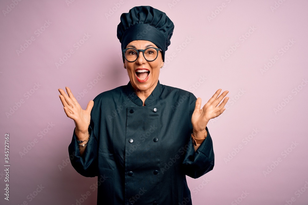 Middle age brunette chef woman wearing cooker uniform and hat over isolated pink background celebrating crazy and amazed for success with arms raised and open eyes screaming excited. Winner concept Middle age brunette chef woman wearing cooker uniform and hat over isolated pink background celebrating crazy and amazed for success with arms raised and open eyes screaming excited. Winner concept
