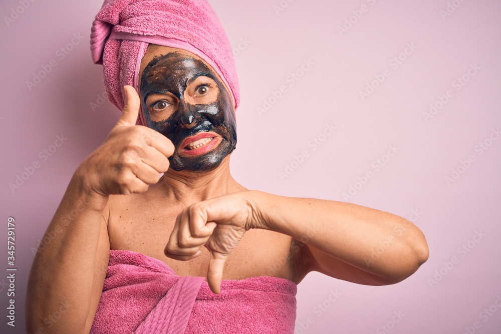 Middle age brunette woman wearing beauty black face mask over isolated pink background Doing thumbs up and down, disagreement and agreement expression. Crazy conflict Middle age brunette woman wearing beauty black face mask over isolated pink background Doing thumbs up and down, disagreement and agreement expression. Crazy conflict