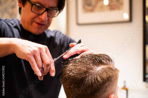 Barber cuts the hair of man with scissors and comb
