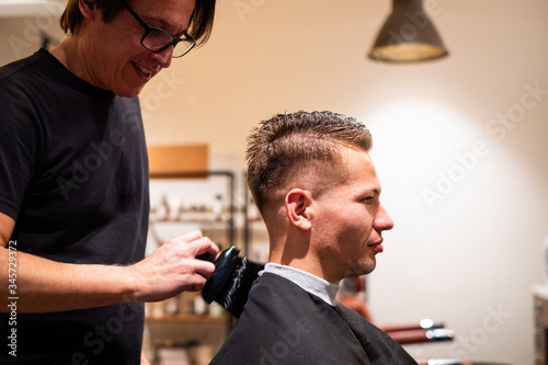 Barber brushes the hair of man after cutting from shoulder