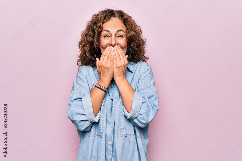 Middle age beautiful woman wearing casual denim shirt standing over pink background laughing and embarrassed giggle covering mouth with hands, gossip and scandal concept Middle age beautiful woman wearing casual denim shirt standing over pink background laughing and embarrassed giggle covering mouth with hands, gossip and scandal concept