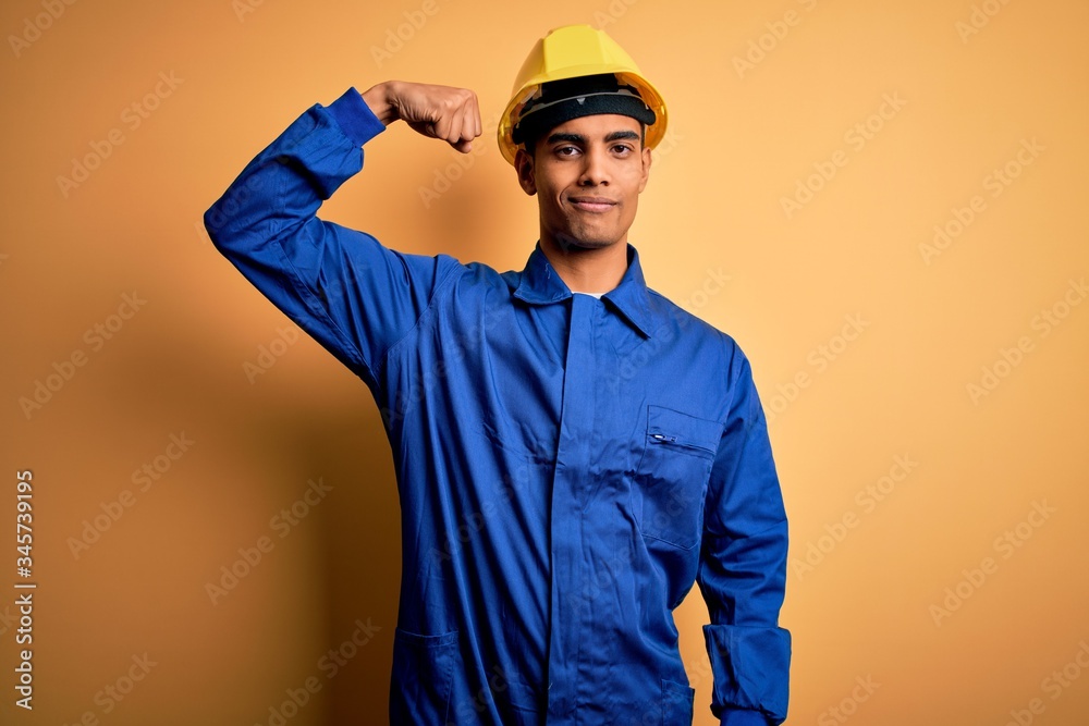 Young handsome african american worker man wearing blue uniform and security helmet Strong person showing arm muscle, confident and proud of power