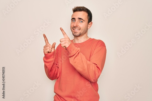 Young handsome man with blue eyes wearing casual sweater standing over white background smiling and looking at the camera pointing with two hands and fingers to the side.