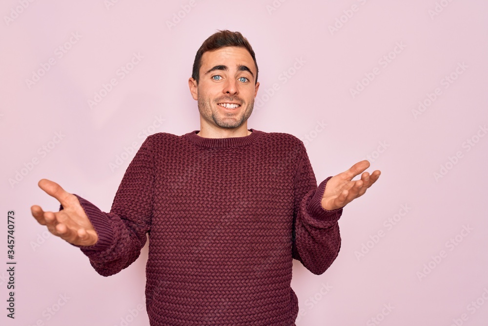 Fototapeta premium Young handsome man with blue eyes wearing casual sweater standing over pink background smiling cheerful with open arms as friendly welcome, positive and confident greetings