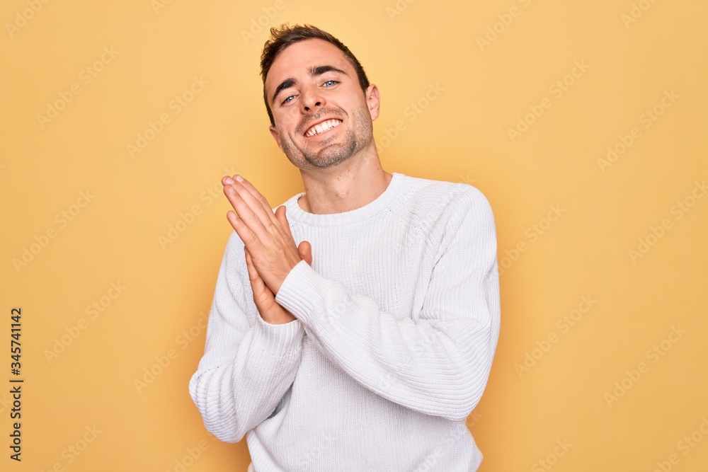 Young handsome man with blue eyes wearing casual sweater standing over yellow background clapping and applauding happy and joyful, smiling proud hands together Young handsome man with blue eyes wearing casual sweater standing over yellow background clapping and applauding happy and joyful, smiling proud hands together