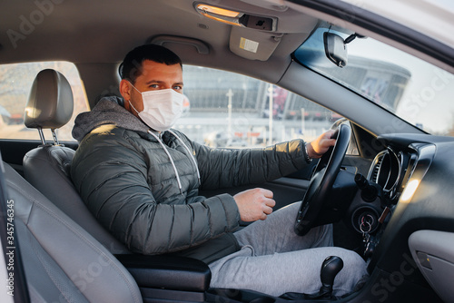 A young man sits behind the wheel wearing a mask for personal safety while driving during a pandemic and coronavirus. Epidemic © Andrii