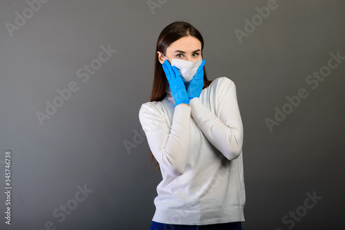 Girl in medical gloves dress a medical mask on her face on a background. Respiratory disease. Covid-19 © Ivan Zelenin