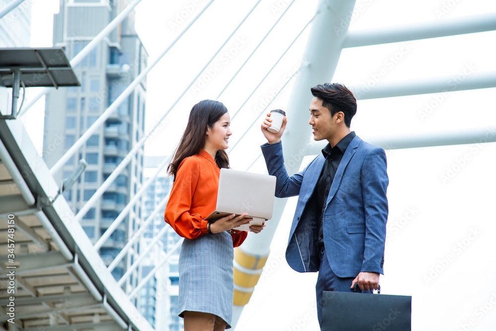 Portrait of young confident Asian Business woman and businessman discussing work and using digital laptop while standing in city outdoor. Portrait of young confident Asian Business woman and businessman discussing work and using digital laptop while standing in city outdoor.