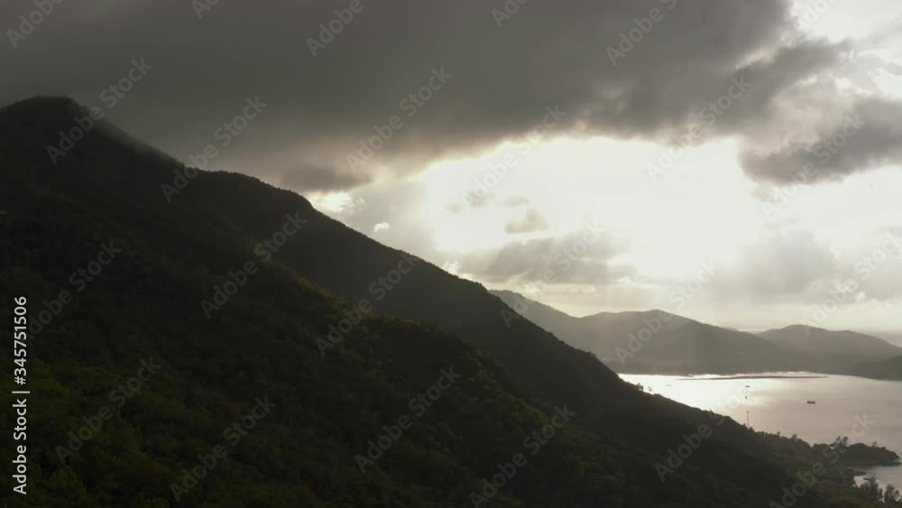 Aerial drone shot along mountain with sea view against sunset flares trough low clouds Aerial drone shot along mountain with sea view against sunset flares trough low clouds