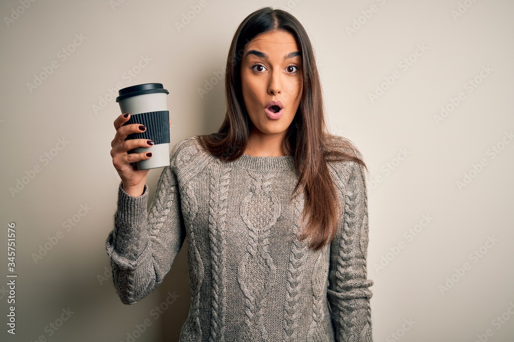 Young beautiful brunette woman drinking glass of coffee over isolated white background scared in shock with a surprise face, afraid and excited with fear expression Young beautiful brunette woman drinking glass of coffee over isolated white background scared in shock with a surprise face, afraid and excited with fear expression