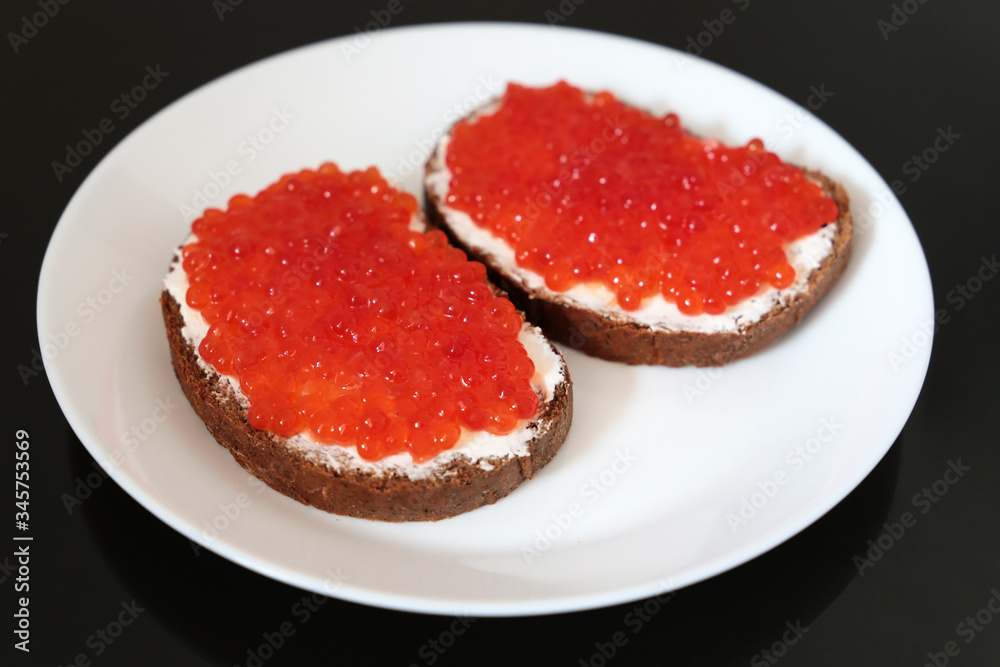 Sandwiches with red caviar, butter and rye bread on white plate, selective focus. Traditional russian dish Sandwiches with red caviar, butter and rye bread on white plate, selective focus. Traditional russian dish