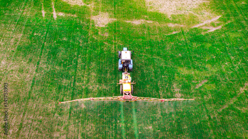 A tractor sprays fertilizers on a spring field. The farmer fertilizes the fields with agricultural machinery. Aerial view.