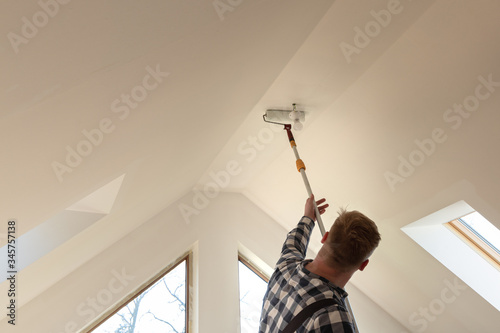 Home improvement concept, handyman painting a wall with a white paint near roof window in attic