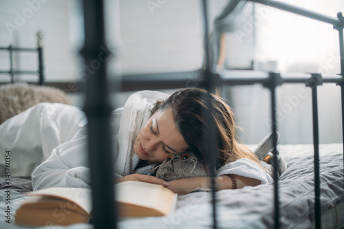 A woman in a bathrobe sleeps on a bed with a book