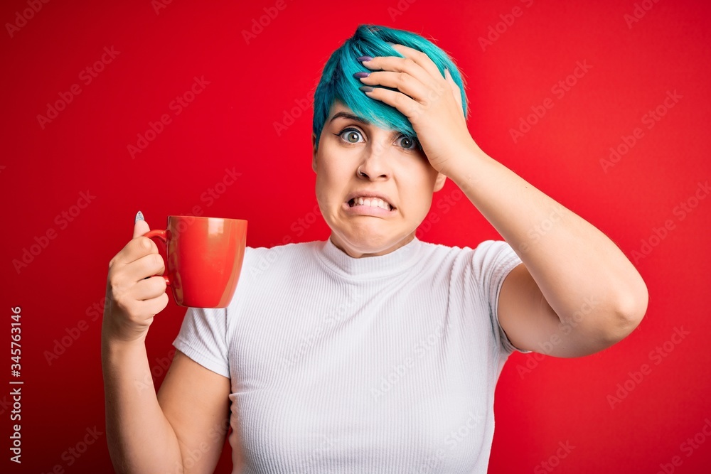 Young woman with blue fashion hair drinking a cup of coffee s over red isolated background stressed with hand on head, shocked with shame and surprise face, angry and frustrated. Fear and upset Young woman with blue fashion hair drinking a cup of coffee s over red isolated background stressed with hand on head, shocked with shame and surprise face, angry and frustrated. Fear and upset