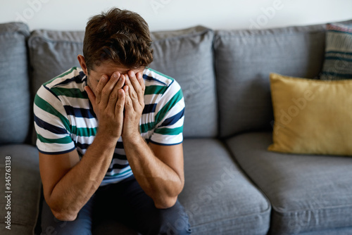 Young man sitting on his sofa looking distraught photo
