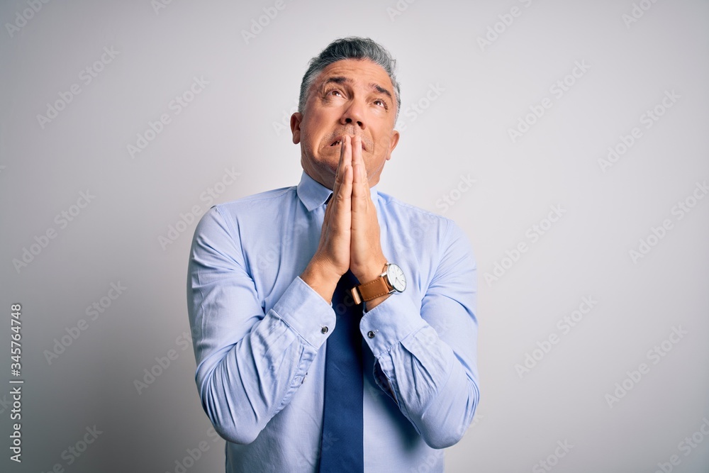 Middle age handsome grey-haired business man wearing elegant shirt and tie begging and praying with hands together with hope expression on face very emotional and worried. Begging.