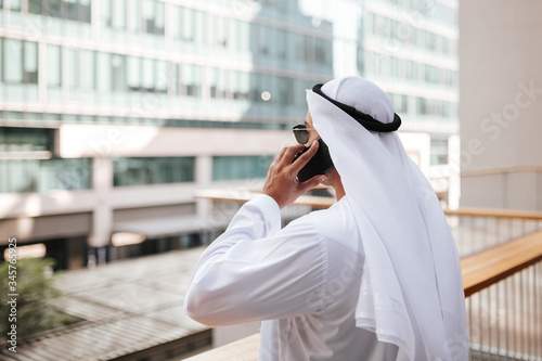Photography Emirati guy wearing traditional kandura in urban city emirates lifestyle talking to smart phone