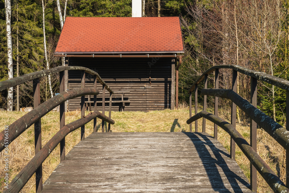 Obraz premium Fisherman's house with a wooden pedestrian bridge on a tiny island in the middle of the lake. Autumn view. Czech Republic