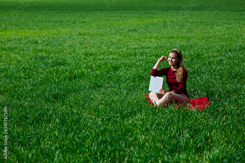 Young successful woman is sitting on green grass with a laptop in her hands. Rest after a good working day. Work on the nature. Student girl working in a secluded place. New business ideas © Дмитрий Ткачук