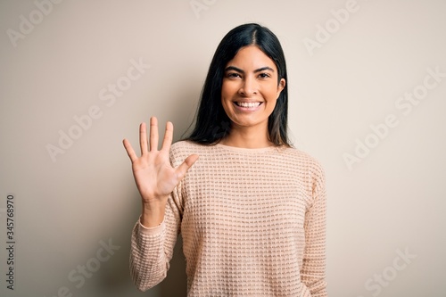Young beautiful hispanic woman wearing elegant pink sweater over isolated background showing and pointing up with fingers number five while smiling confident and happy.