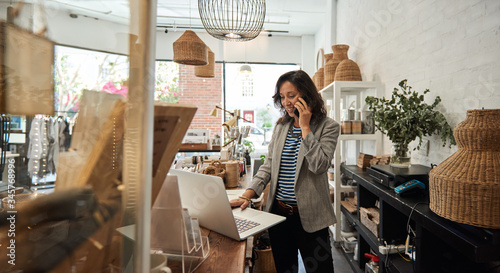 Smiling Asian woman talking on a cellphone in her store photo