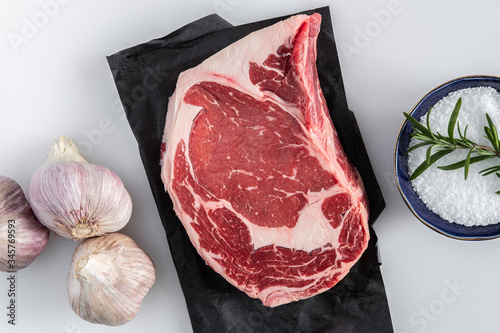 A photograph of a boneless rib eye steak with garlic, kosher salt and rosemary on a butcher cutting board photo