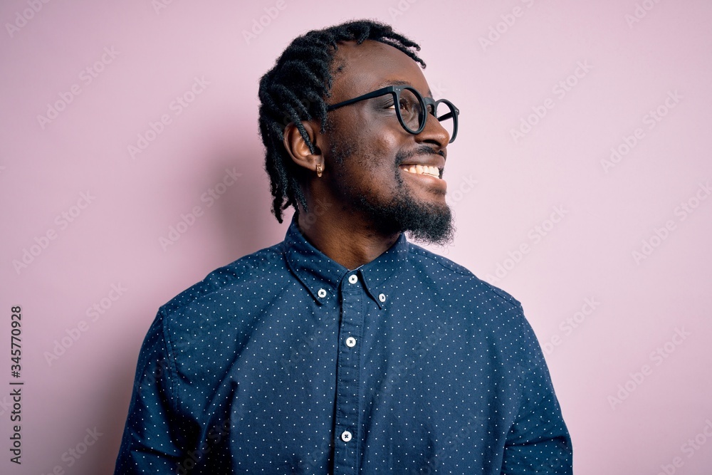 Obraz premium Young handsome african american man wearing casual shirt and glasses over pink background looking away to side with smile on face, natural expression. Laughing confident.