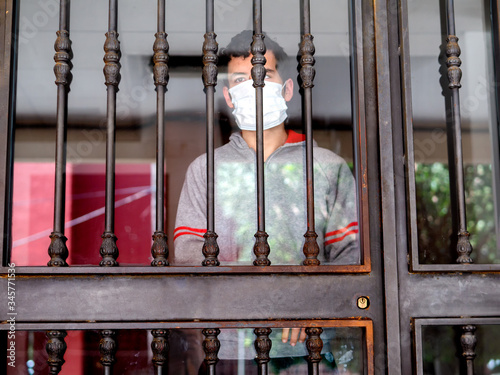 Man with a medical mask looks sadly out of the door during his confinement because of convid 19 photo