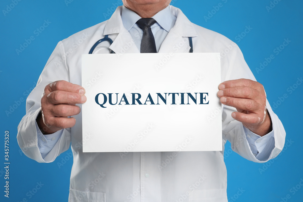 Doctor holding sign with text QUARANTINE on blue background, closeup. Stay at home during coronavirus outbreak Doctor holding sign with text QUARANTINE on blue background, closeup. Stay at home during coronavirus outbreak