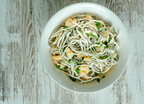 Foto Bol blanco de gulas con gambas, ajos, perejil, guindillas sobre mesa blanca