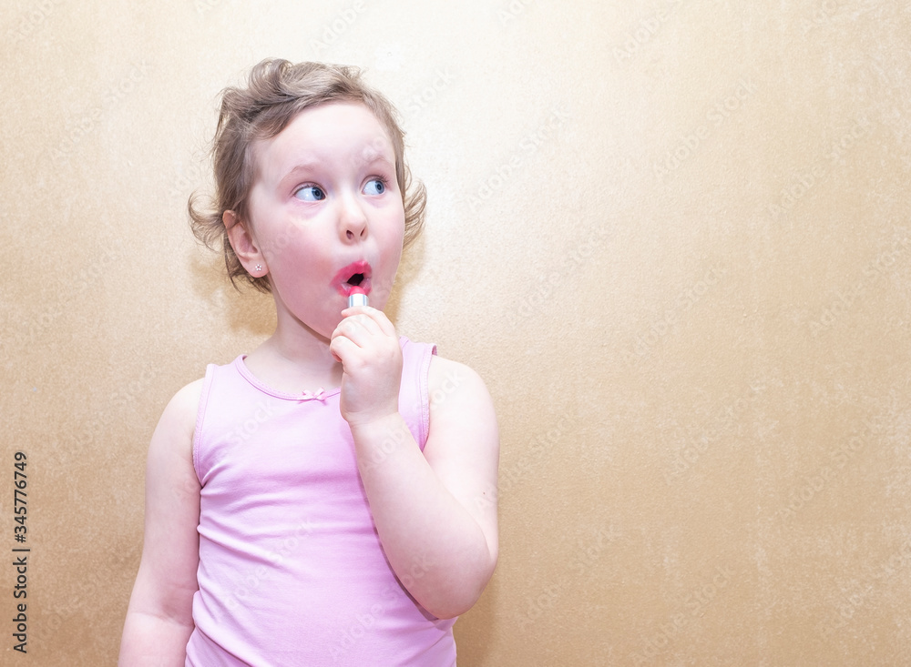 A child, a girl, paints her lips with red lipstick. Emotional portrait of a girl. Copy space A child, a girl, paints her lips with red lipstick. Emotional portrait of a girl. Copy space