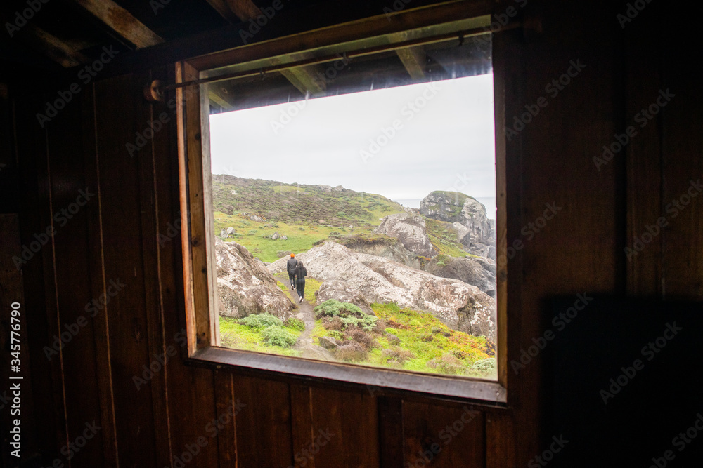 Two people hiking through a rocky landscape seen through the window of a cabin. Two people hiking through a rocky landscape seen through the window of a cabin.