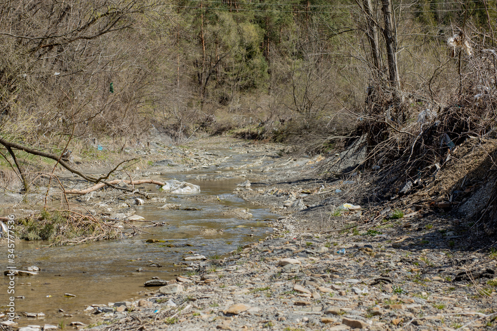A beautiful small stream is littered with a bunch of garbage, empty bottles, cellophane bags, plastic cans A beautiful small stream is littered with a bunch of garbage, empty bottles, cellophane bags, plastic cans