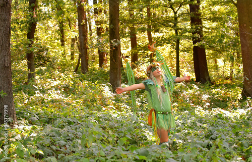 A young girl is dressed up as a fairy.
She is seen in a forest with a large
decorated wreath on her head.