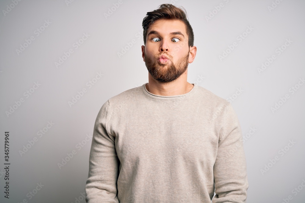 Young handsome blond man with beard and blue eyes wearing casual sweater making fish face with lips, crazy and comical gesture. Funny expression. Young handsome blond man with beard and blue eyes wearing casual sweater making fish face with lips, crazy and comical gesture. Funny expression.