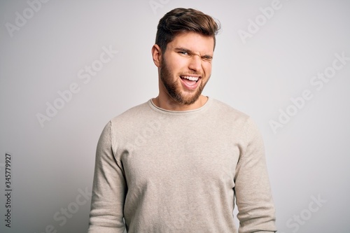 Young handsome blond man with beard and blue eyes wearing casual sweater winking looking at the camera with sexy expression, cheerful and happy face.