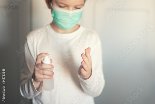 a boy in a medical mask disinfects his hands with a spray photo